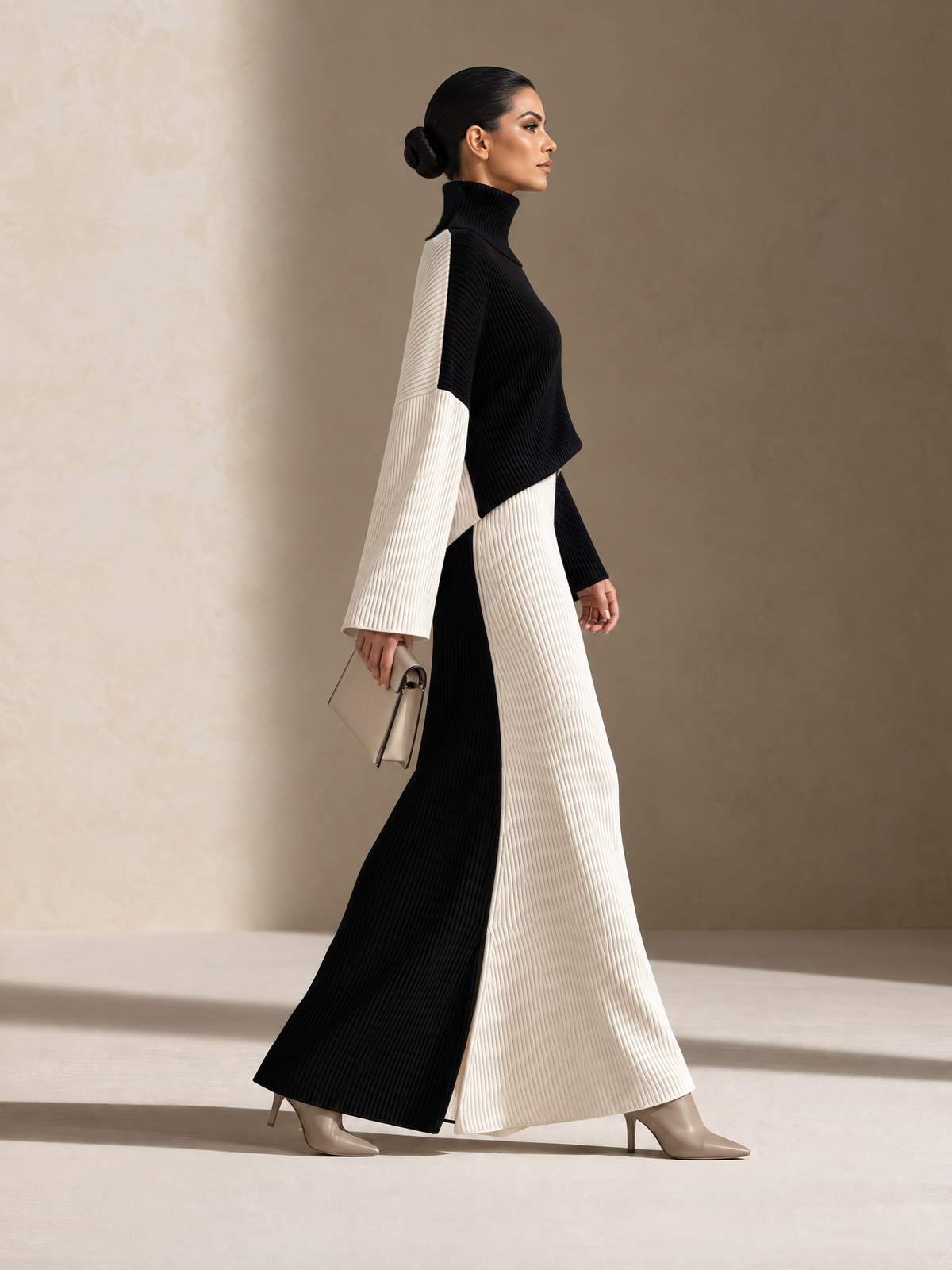 Side view of a women's black-and-white colorblock ribbed knit maxi set featuring a high turtleneck, contrasting long sleeves, and a floor-length flared skirt with an elegant, elongated silhouette.