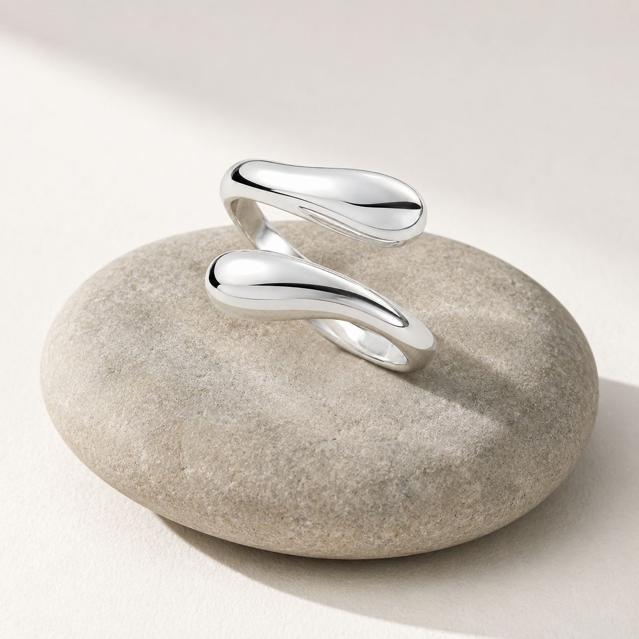 Sterling silver water drop adjustable ring resting on a smooth pebble in soft natural light